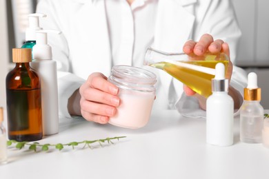 Photo of Dermatologist developing cosmetic product at white table indoors, closeup