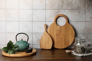 Wooden cutting boards, kettle and tea on table near tiled wall. Space for text