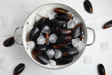 Colander with raw mussels and ice on white marble table, flat lay