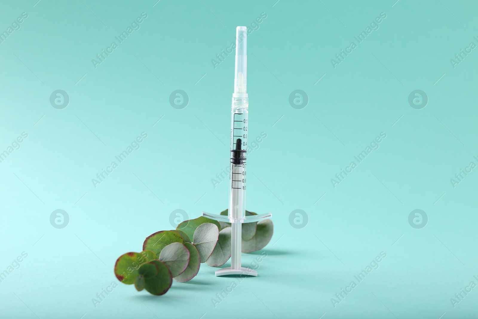 Photo of Cosmetology. Medical syringe and eucalyptus branch on turquoise background