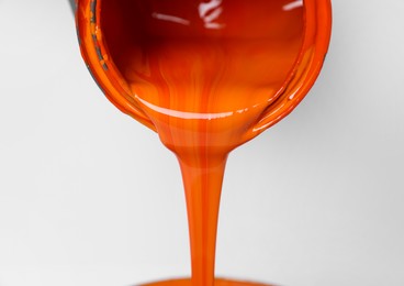 Photo of Pouring orange paint from can on white background, closeup