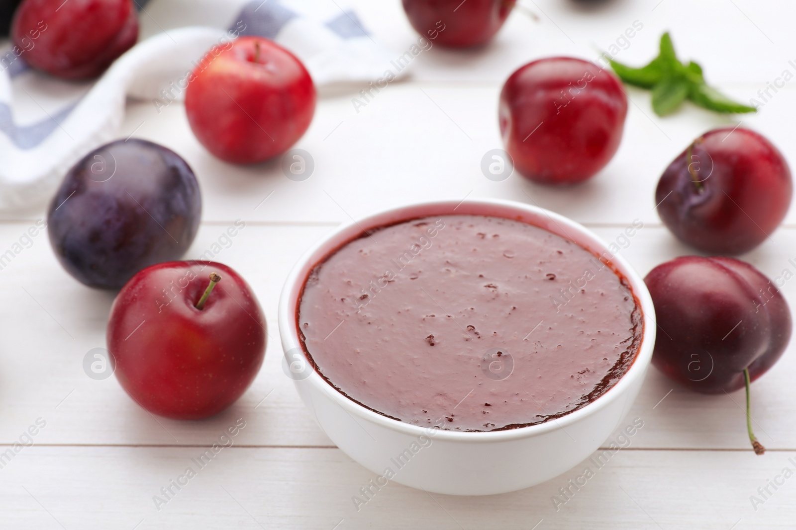 Photo of Plum puree in bowl and fresh fruits on white wooden table