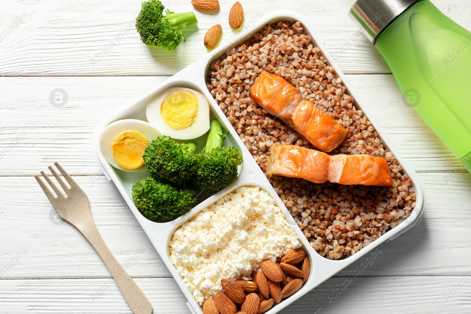 Photo of Container with natural healthy lunch and bottle of water on table. High protein food