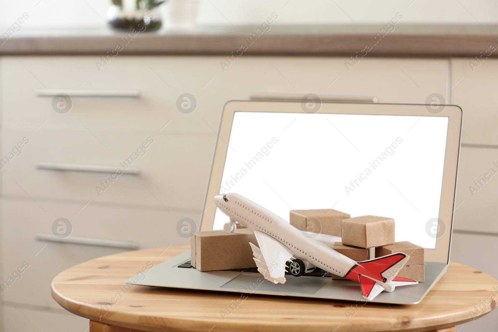 Photo of Laptop and plane model with boxes on table indoors. Courier service