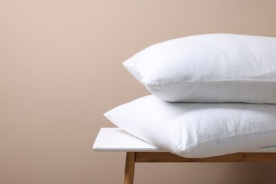 Photo of Stack of soft white pillows on table near beige wall. Space for text