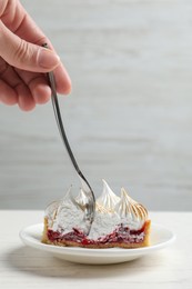 Woman eating delicious tartlet dessert with meringue and jam at white table, closeup