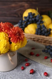 Photo of Bouquet of beautiful chrysanthemum flowers and rose hip berries on grey table