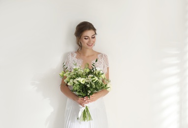 Photo of Young bride wearing wedding dress with beautiful bouquet on light background