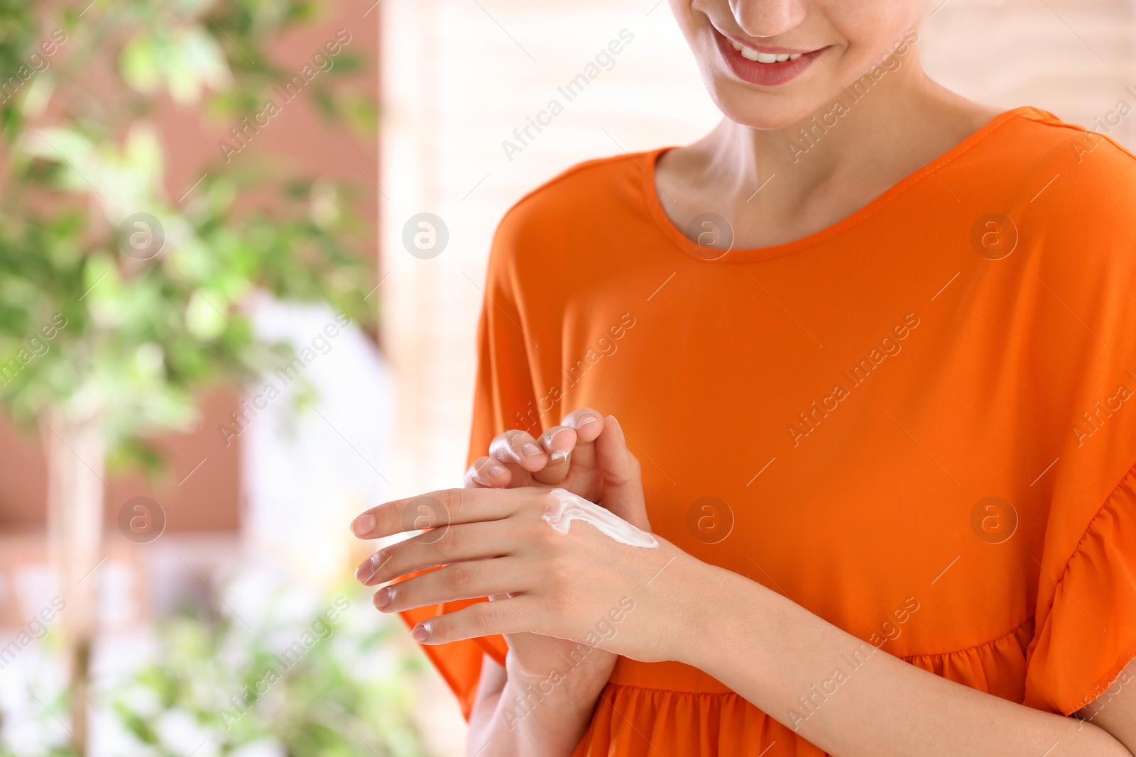 Photo of Young woman applying cream on her hands indoors, closeup