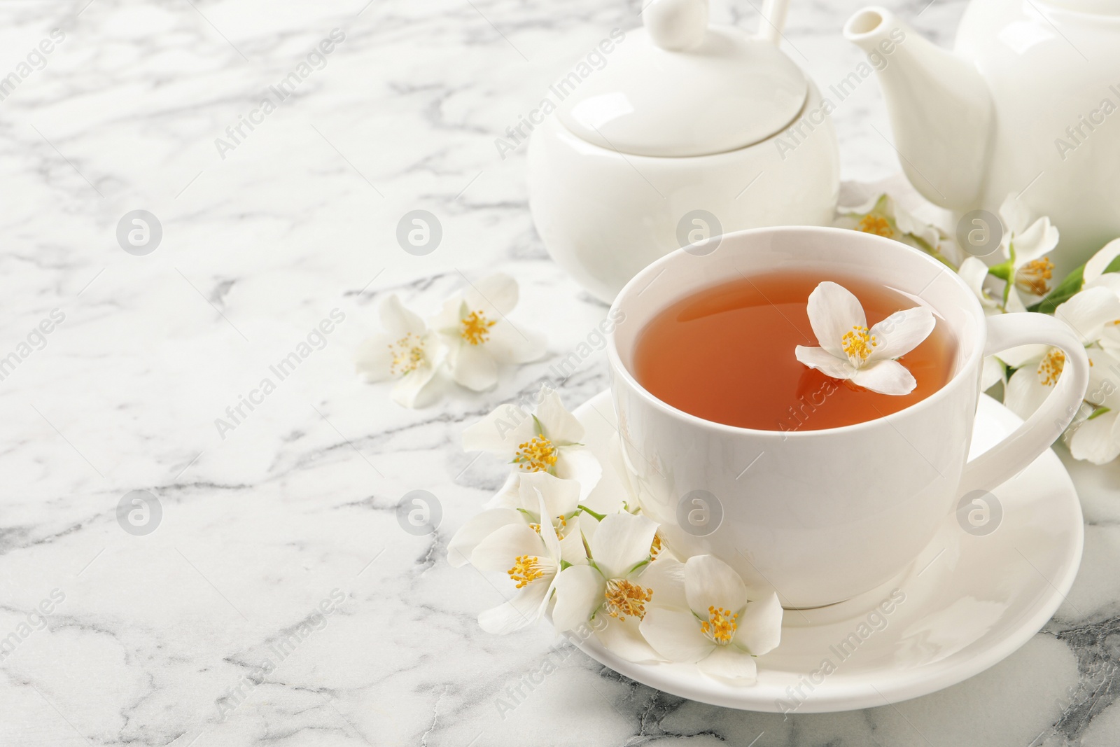 Photo of Aromatic jasmine tea and fresh flowers on white marble table, space for text