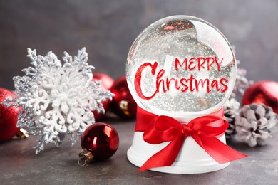 Image of Beautiful snow globe with phrase Merry Christmas and festive decor on grey table