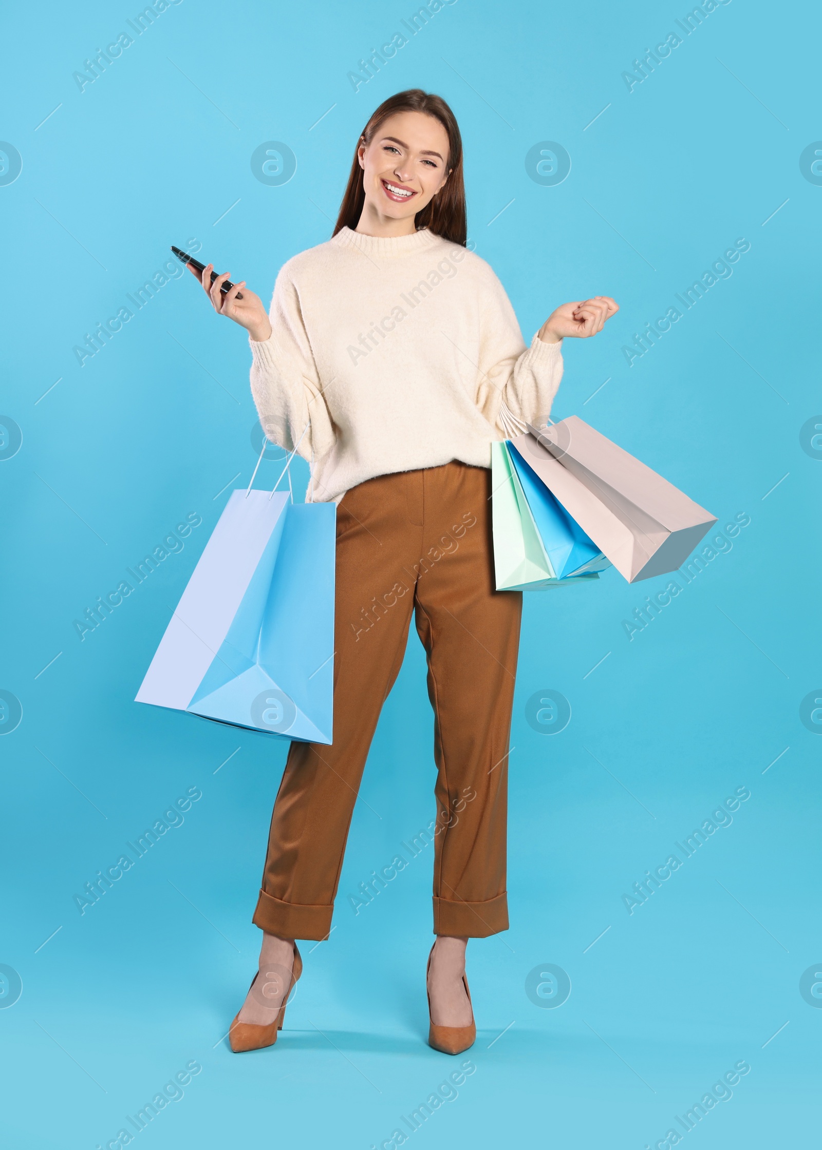 Photo of Happy young woman with shopping bags and smartphone on light blue background. Big sale