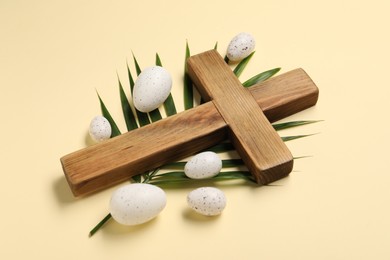 Photo of Wooden cross, painted Easter eggs and palm leaf on beige background