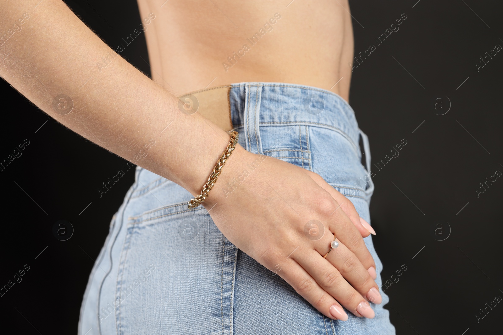 Photo of Woman wearing stylish metal chain on her wrist and ring against black background, closeup. Luxury jewelry