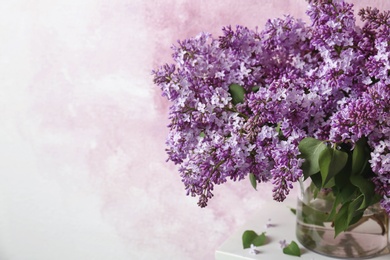 Vase with blossoming lilac on table against color background. Spring flowers