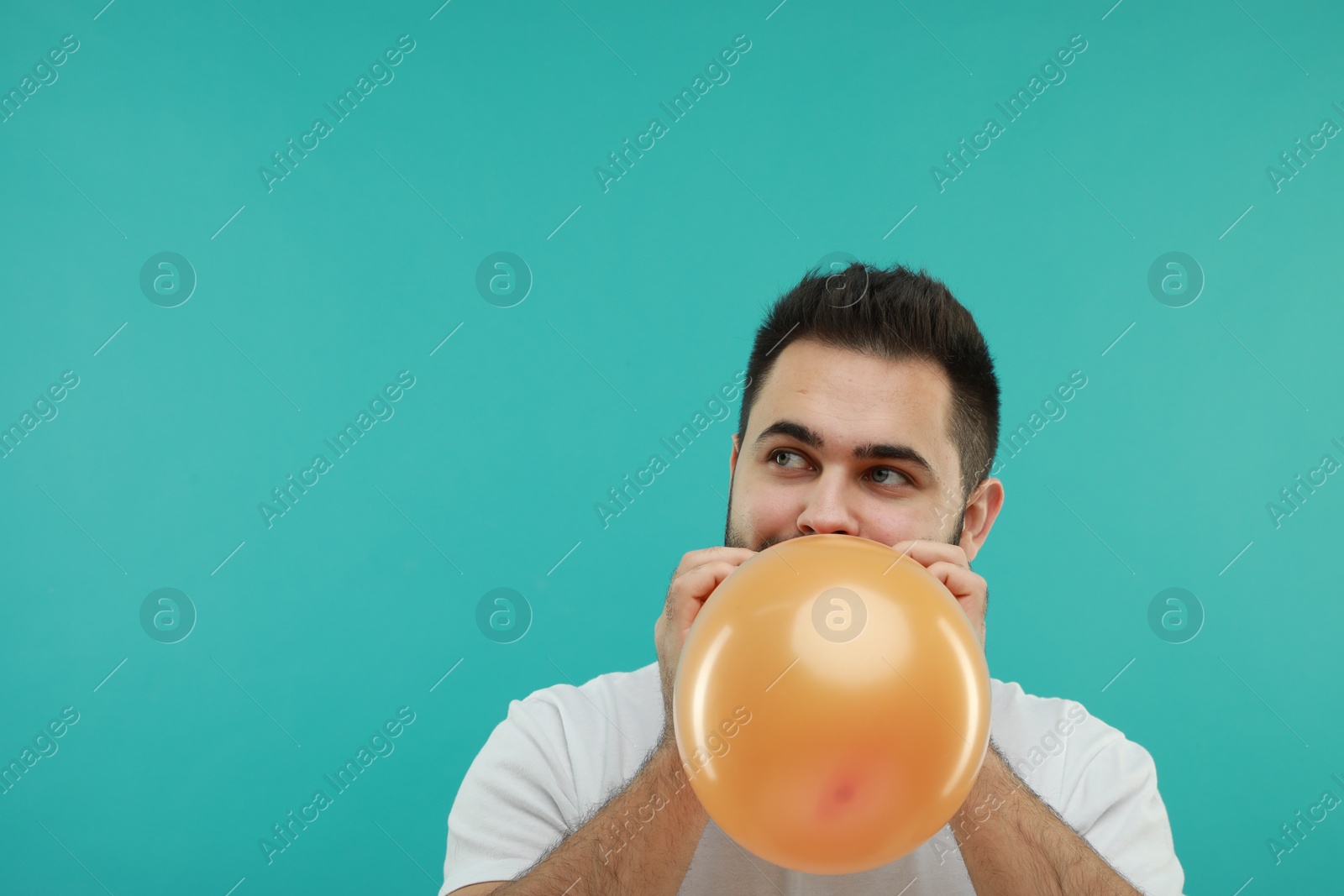 Photo of Man inflating bright balloon on turquoise background, space for text