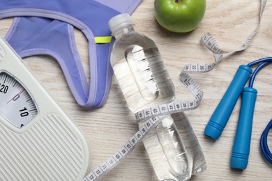 Photo of Weight loss concept. Flat lay composition with bottle of water, measuring tape and skipping rope on white wooden table