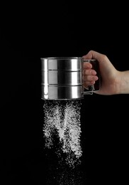 Photo of Woman sieving flour against black background, closeup. Space for text