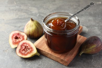 Photo of Jar of tasty sweet jam and fresh figs on grey table