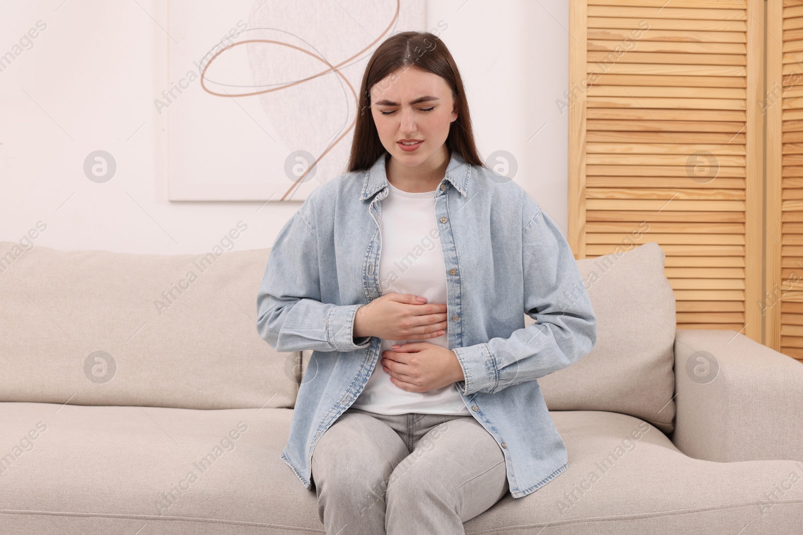 Photo of Young woman suffering from stomach pain at home