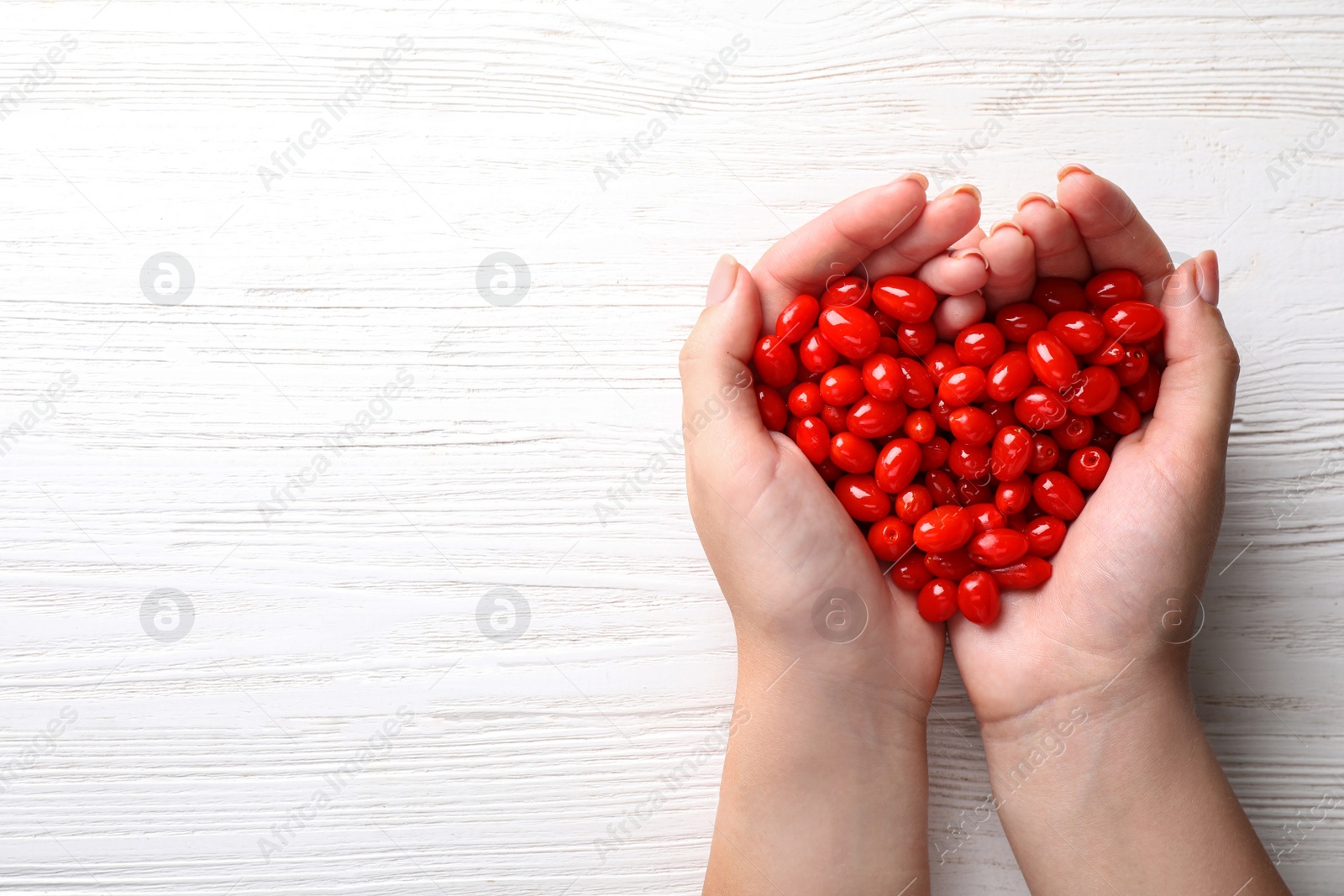 Photo of Woman holding pile of fresh ripe goji berries over white wooden table, top view. Space for text