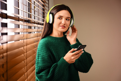 Young woman listening to audiobook near window indoors