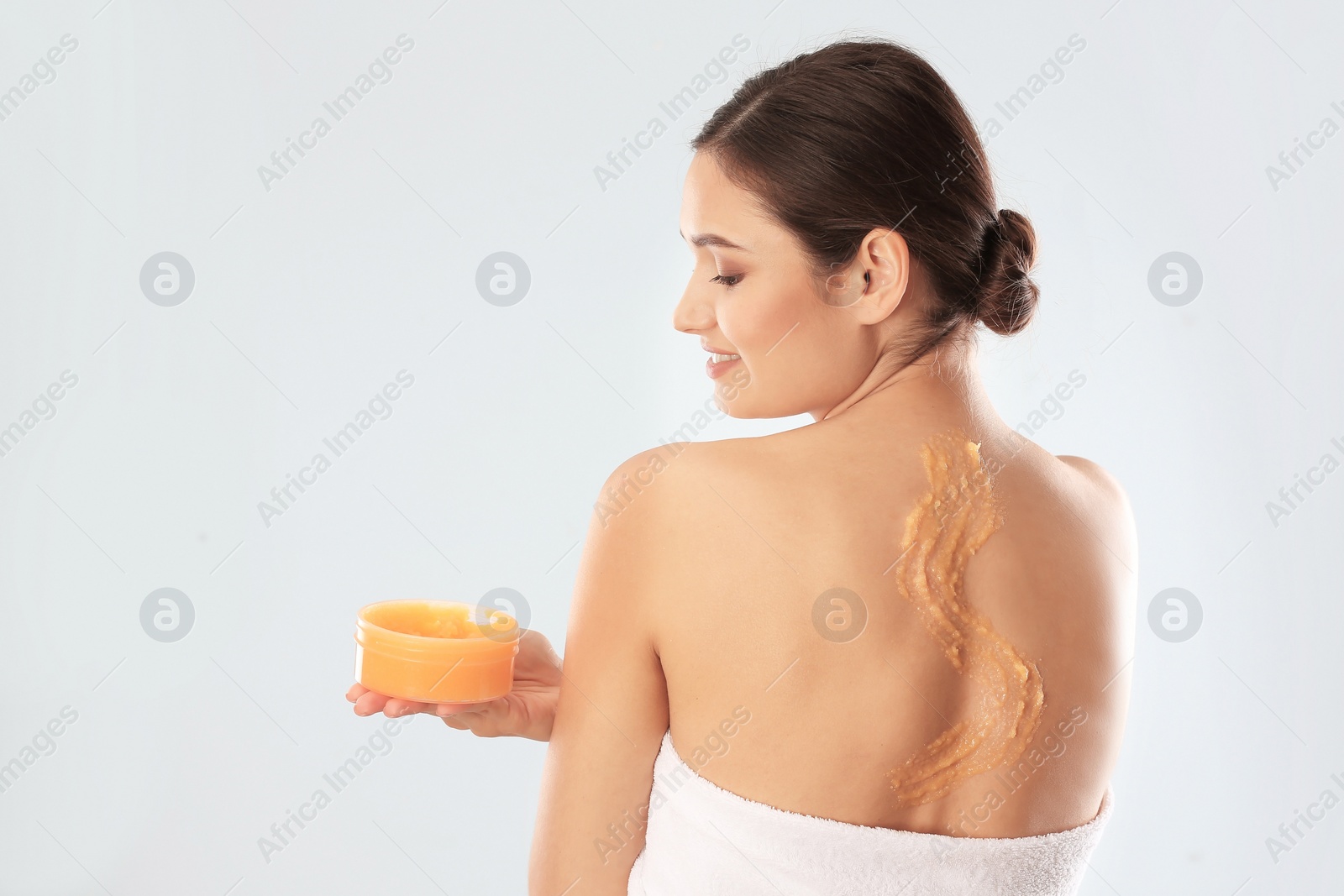 Photo of Young woman applying natural scrub on her body against light background