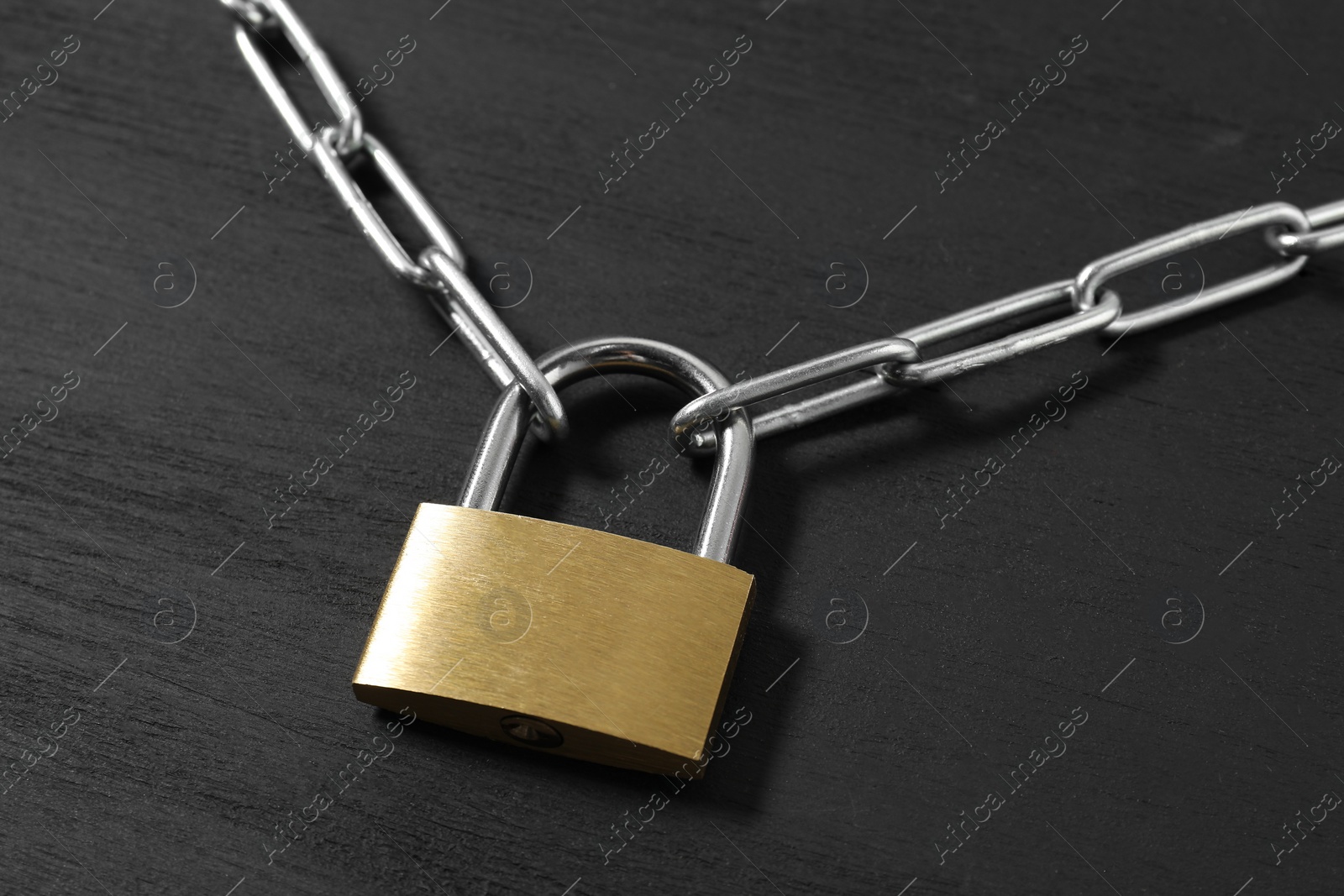 Photo of Steel padlock with chain on black wooden table, closeup