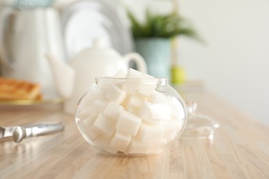 Glass bowl with white sugar cubes on wooden table