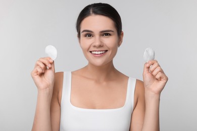 Young woman with cotton pads on light grey background