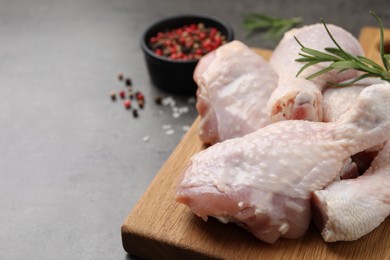 Photo of Raw chicken drumsticks with rosemary and spices on grey table, closeup. Space for text
