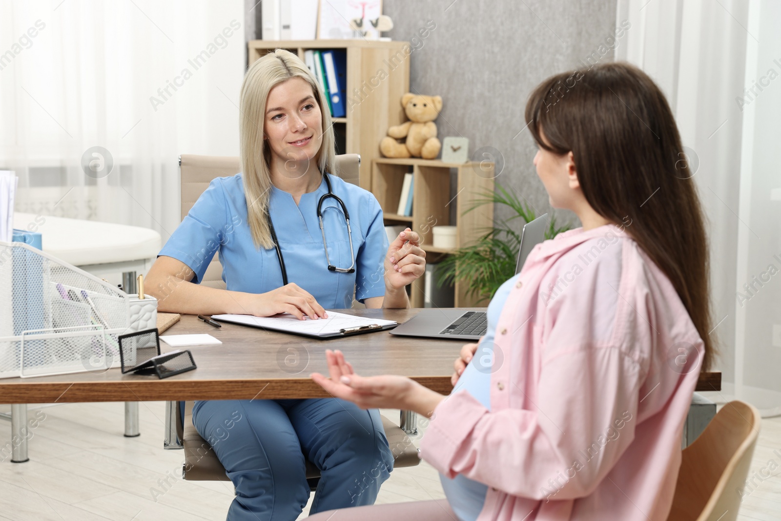 Photo of Doctor consulting pregnant patient at table in clinic