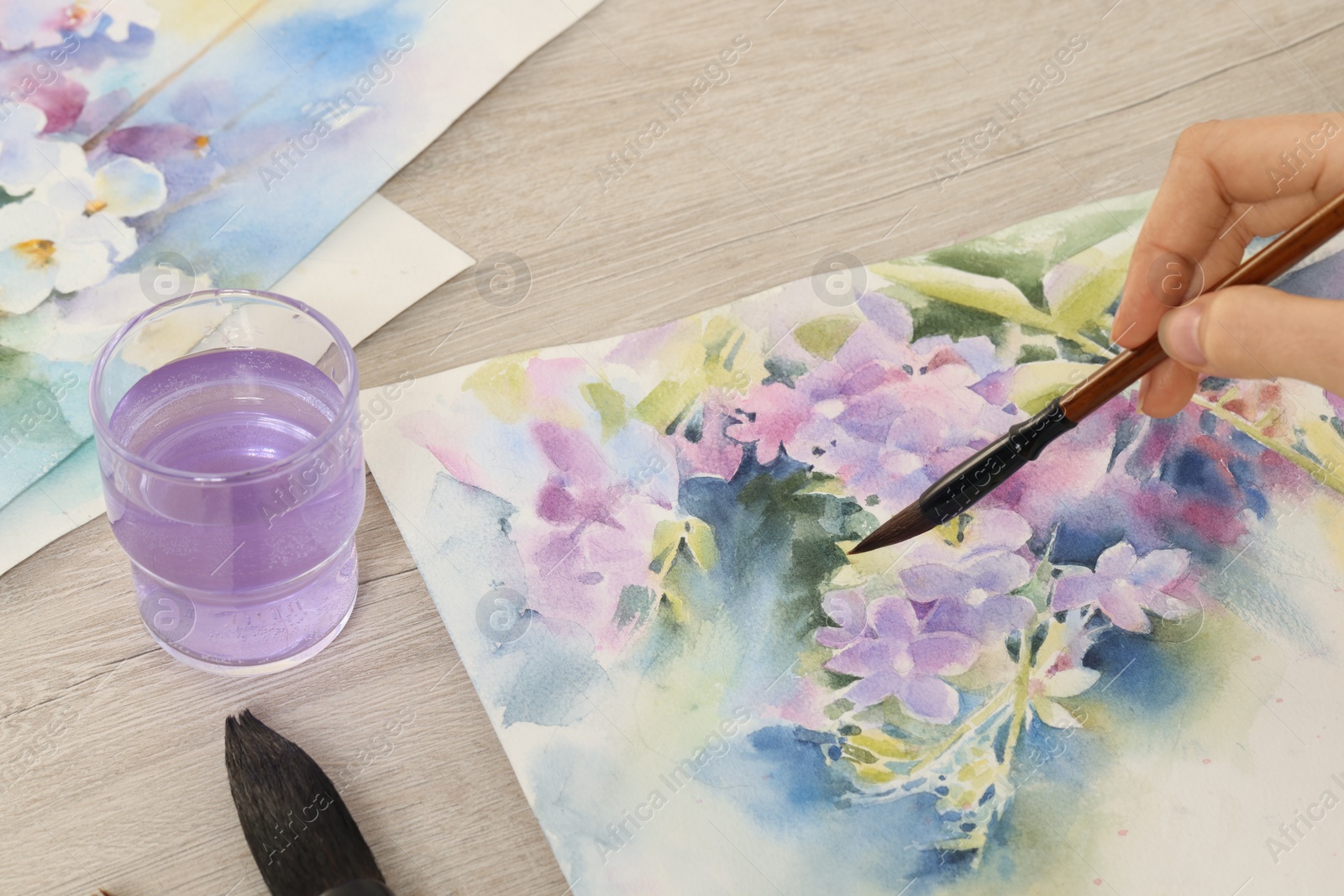 Photo of Woman painting flowers with watercolor at white wooden table, closeup. Creative artwork