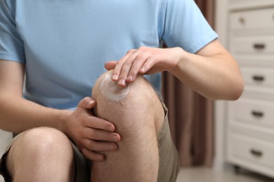 Photo of Man applying ointment onto his knee indoors, closeup