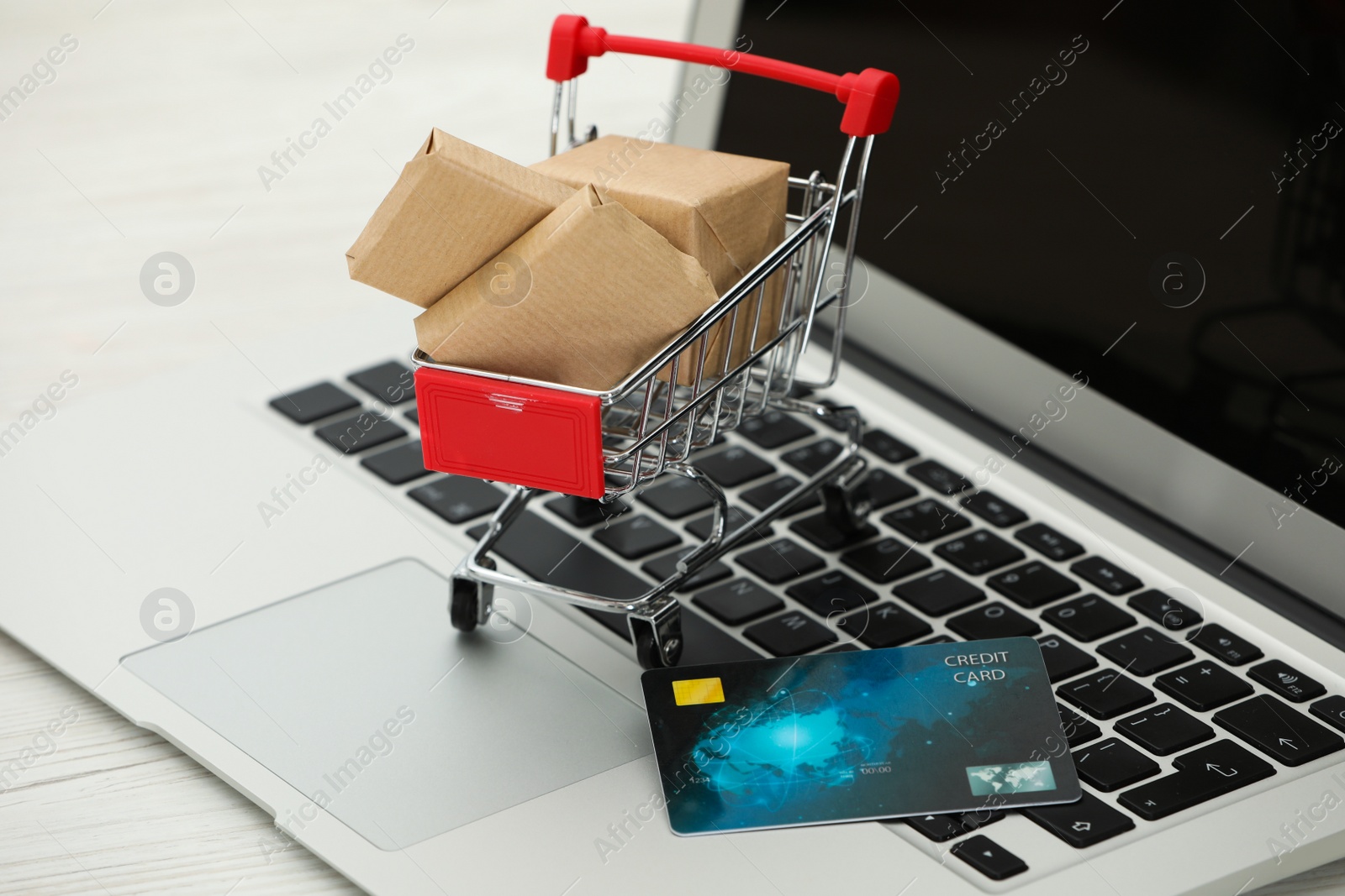 Photo of Online payment concept. Small shopping cart with bank card, boxes on laptop, closeup