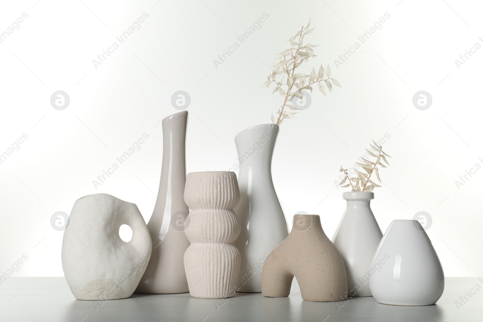 Photo of Different stylish vases and dried flowers on light table against white background