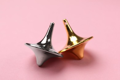 Photo of Golden and silver spinning tops on pink background, closeup