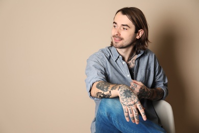 Photo of Young man with tattoos on body against beige background. Space for text