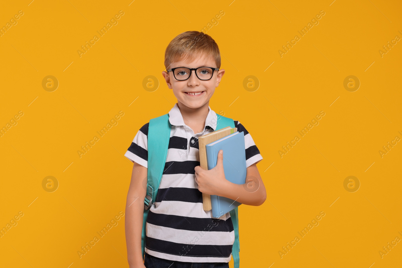 Photo of Happy schoolboy in glasses with backpack and books on orange background