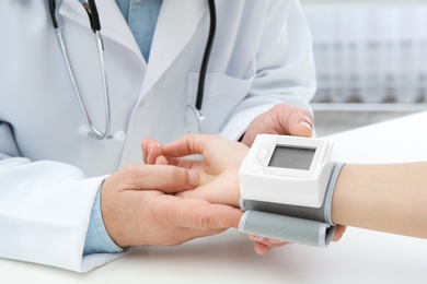 Doctor checking young woman's pulse with medical device at table in hospital, closeup