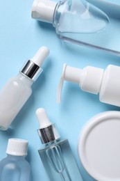 Photo of Many different bottles of cosmetic serum on light blue background, flat lay