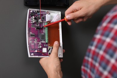 Photo of Man installing home security alarm system on gray wall indoors, closeup