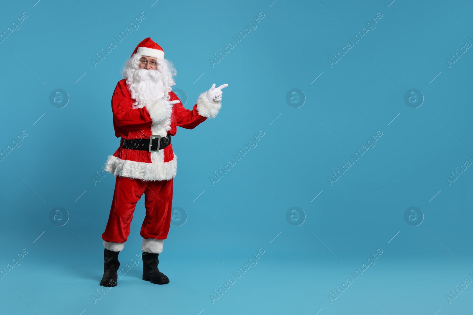 Photo of Merry Christmas. Santa Claus pointing at something on light blue background, space for text