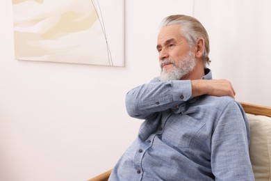 Senior man suffering from pain in his shoulder at home, space for text. Arthritis symptoms