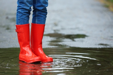 Photo of Woman with red rubber boots in puddle, closeup. Rainy weather