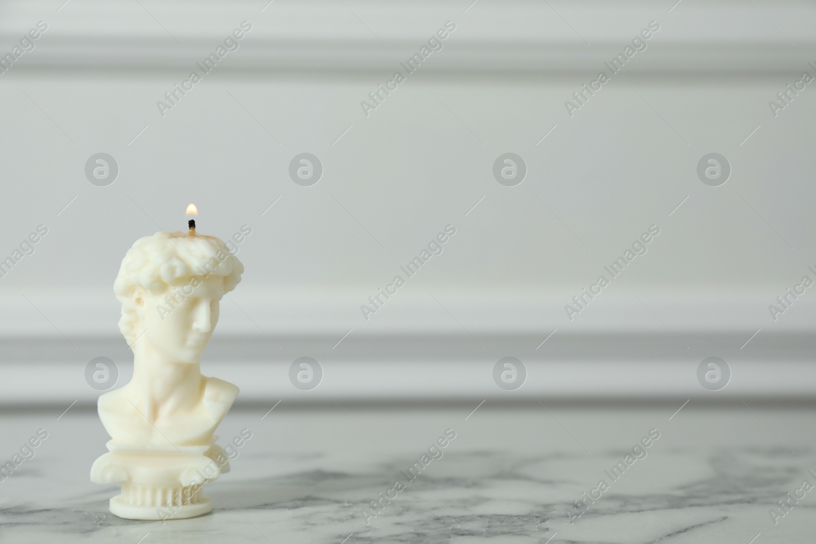 Photo of Stylish David bust candle on white marble table. Space for text