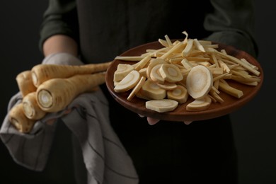 Photo of Woman holding whole and cut parsnips on black background, closeup