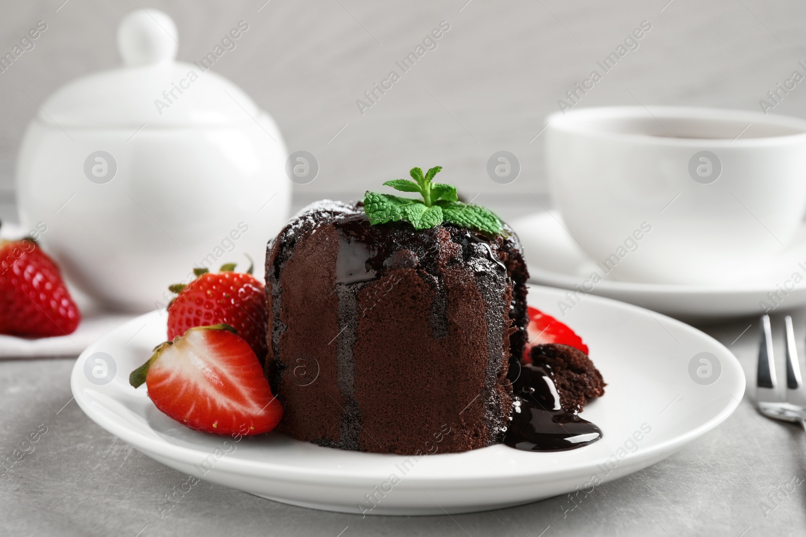 Photo of Delicious warm chocolate lava cake with mint and strawberries on table