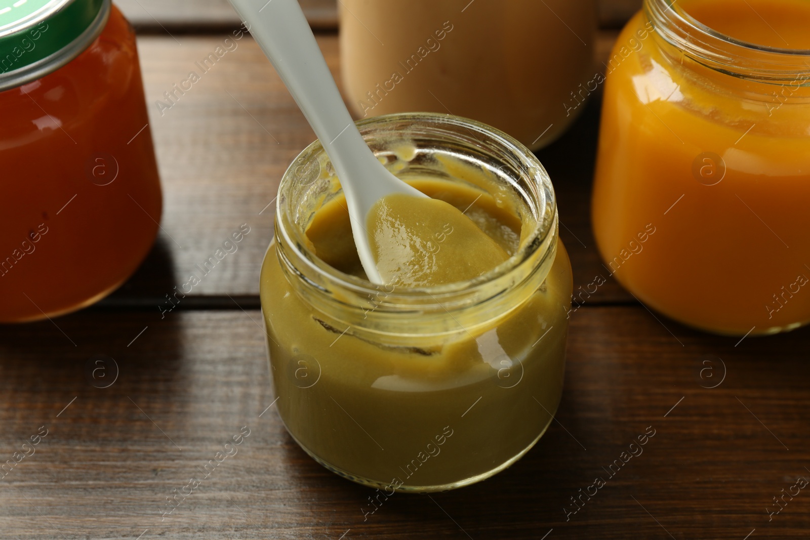 Photo of Tasty baby food in jar and spoon on wooden table, closeup