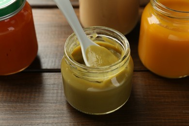 Tasty baby food in jar and spoon on wooden table, closeup